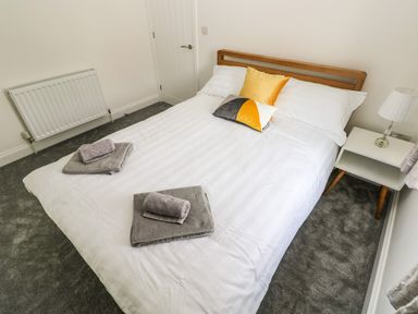 A bedroom with a double bed white bedding two grey towels on the bed a small white bedside table with a lamp and a radiator on the wall at Larkhill in Tenby