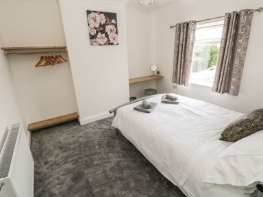 A bedroom with a bed with towels on it a window with curtains a wall-mounted shelf with hangers a small desk area and carpeted floor at Larkhill in Tenby