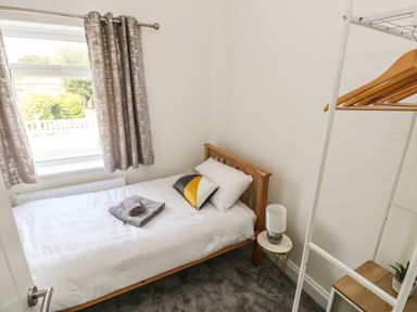 A small bedroom with a single bed bedside table with lamp window with curtains and an open wardrobe at Larkhill in Tenby
