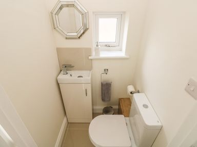 A small bathroom with a toilet a sink with cabinet a mirror a window and a towel at Larkhill in Tenby