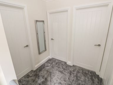 A hallway with three white doors a rectangular mirror on the wall and grey carpet at Larkhill in Tenby