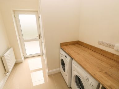 A laundry room with a wooden countertop over a washer and dryer and a door with frosted glass at Larkhill in Tenby