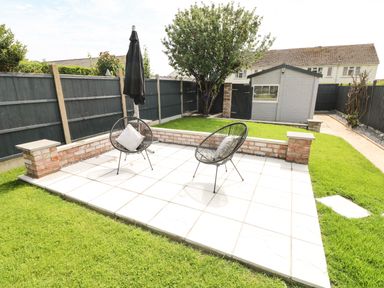A backyard patio with two chairs and an umbrella near a small shed and a tree at Larkhill in Tenby