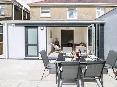 A patio with a dining table and chairs set with plates and drinks outside a house with large folding doors at Larkhill in Tenby
