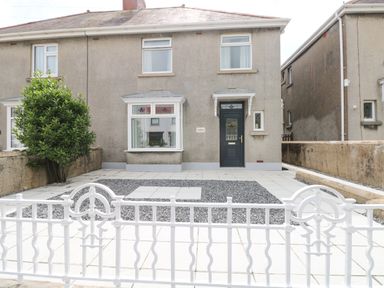 Front view of a two story house with a paved and gravel yard and a white metal gate at Larkhill in Tenby
