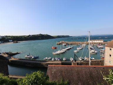 A harbor with boats docked near a stone pier and hillside in the background at Larkhill in Tenby
