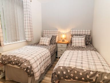 A bedroom with two single beds with polka dot and plaid bedding a nightstand and lamp at Lavender Lodge in St Ann's Chapel Cornwall