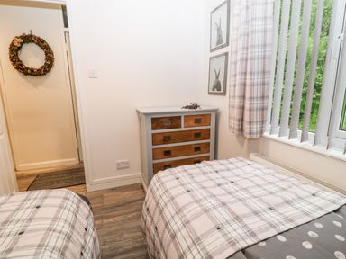 A bedroom with two beds a chest of drawers and a window with curtains at Lavender Lodge in St Ann's Chapel Cornwall