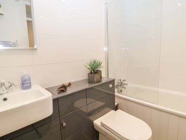 A bathroom with a sink and faucet soap dispenser toilet bathtub and a plant on grey cabinet at Lavender Lodge in St Ann's Chapel Cornwall