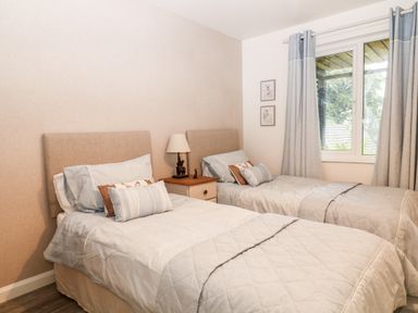 A bedroom with two single beds a nightstand with a lamp and a window with curtains at Lavender Lodge in St  Anns Chapel Cornwall