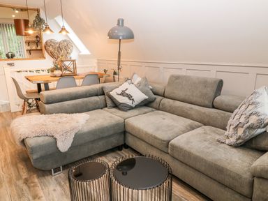 A living room with a gray sectional sofa, two round black coffee tables, a wooden dining table with gray chairs, a floor lamp, and wall decorations at Lavender Lodge in St Ann's Chapel Cornwall