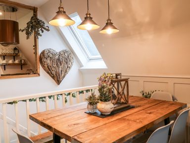 A dining area with a wooden table brown chairs pendant lights and a heart-shaped wood wall decoration at Lavender Lodge in St Ann's Chapel Cornwall
