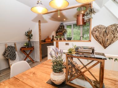 A dining area with wooden table and decorative plants next to a kitchen with cabinets and shelves at Lavender Lodge in St Ann's Chapel Cornwall