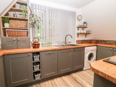 A kitchen with grey cabinets wooden countertops shelves with baskets a washing machine and a sink at Lavender Lodge in St Ann's Chapel Cornwall