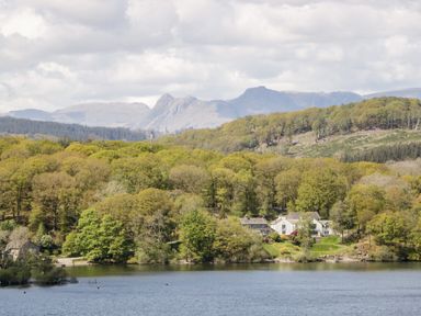 A lake with trees and houses along the shore and mountains in the background at Rose Cottage in Burneside