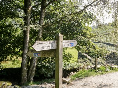 A wooden signpost on a dirt path with directions to Grasmere and Ambleside surrounded by trees and stone walls at Rose Cottage in Burneside
