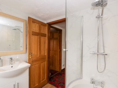 A bathroom with a curved glass shower screen a modern shower head a white sink with a mirror and wooden doors at Rose Cottage in Burneside