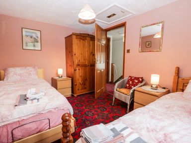 A bedroom with two single beds a wooden wardrobe a wicker chair nightstands with lamps and a patterned red carpet at Rose Cottage in Burneside