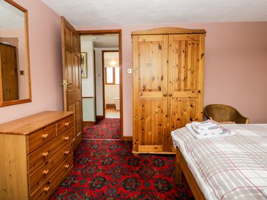 A bedroom with a wooden wardrobe chest of drawers and bed with folded towels at Rose Cottage in Burneside