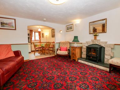 A living room with a red patterned carpet a leather sofa armchair fireplace and a dining table seen through an archway at Rose Cottage Burneside