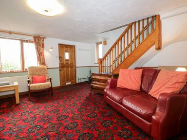 A living room with a red sofa and patterned carpet at Rose Cottage in Burneside