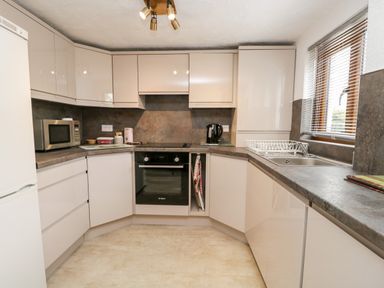 A kitchen with white cabinets gray countertops a microwave oven and a sink with a window at Rose Cottage in Burneside