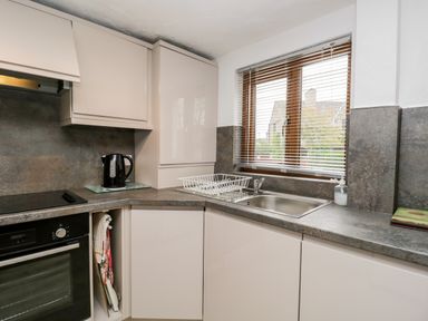 A kitchen with a sink a black kettle a dish drying rack and a window with blinds at Rose Cottage in Burneside