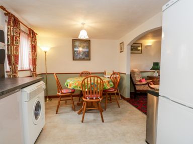A dining area with a round table and wooden chairs next to a washing machine and refrigerator at Rose Cottage in Burneside