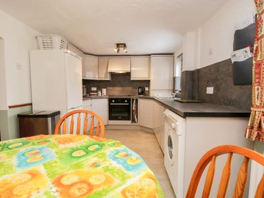 A kitchen with white cabinets a washing machine a refrigerator and a table with wooden chairs at Rose Cottage Burneside