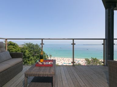 A balcony with wicker furniture a table with champagne glasses and bottle overlooking a beach and sea at Crystal Bay in St Ives