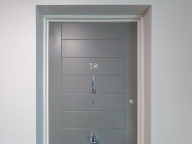 A gray door with the number 12 a door knocker a peephole and a lock in a white wall at Crystal Bay in St Ives