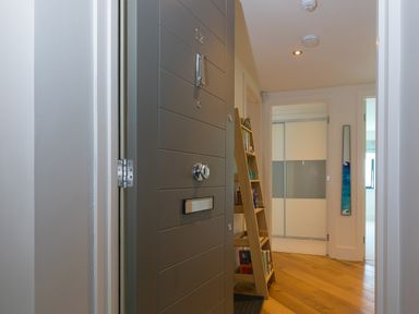 An open grey front door leading to a hallway with wooden floor a leaning wooden bookshelf and white doors at Crystal Bay in St Ives