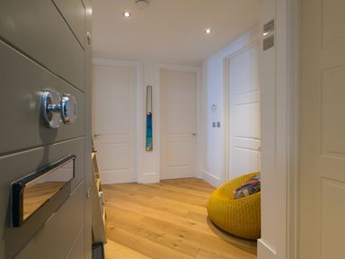 A hallway with three white doors a yellow round chair with a pillow and wooden floor at Crystal Bay in St Ives