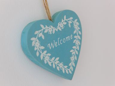 A blue heart shaped wooden sign with white floral decoration and the word Welcome hanging on a wall at Crystal Bay in St Ives