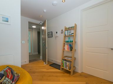 An open door in a room with a wooden floor a ladder bookshelf with books and decorative items a yellow chair with a cushion and a closed white door at Crystal Bay in St Ives