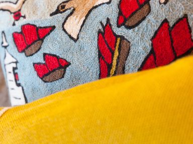 A close up of a textured cushion with red boat designs and a yellow fabric in the foreground