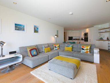 A living room with gray sectional sofa and multicolored pillows adjacent to an open kitchen at Crystal Bay in St Ives