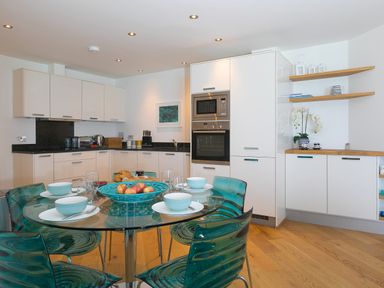 A kitchen with white cabinets glass dining table with blue bowls and chairs at Crystal Bay in St Ives