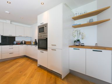 A kitchen with white cabinets wooden shelves with cups and a flowerpot on a countertop at Crystal Bay in St Ives