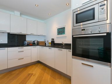 A kitchen with white cabinets wooden floor built in oven microwave toaster and kettle at Crystal Bay in St Ives