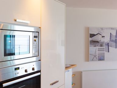 A kitchen with built in stainless steel microwave and oven and a collage of coastal photos on the wall at Crystal Bay in St Ives