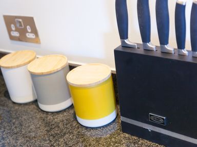 Kitchen countertop with three storage containers with wooden lids and a black knife block with knives at Crystal Bay in St Ives