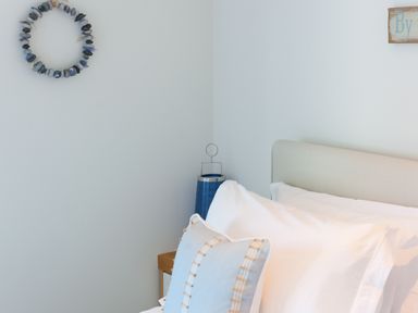 A bedroom corner with a bed pillow a blue lantern on a bedside table and a decorative wreath on the wall at Crystal Bay in St Ives