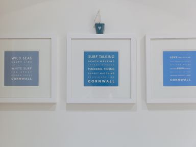 Three framed blue and white text prints on a white wall with a small sailboat decoration on top of the middle frame at Crystal Bay in St Ives