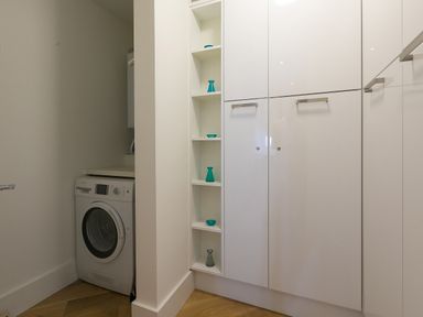 A laundry room with a washing machine and white cabinets with small decorative objects at Crystal Bay in St Ives
