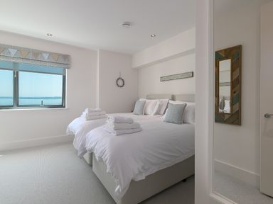 A bedroom with two single beds with white bedding and towels on top and a window with a sea view at Crystal Bay in St Ives