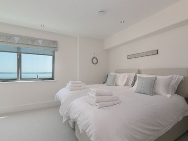 A bedroom with two beds and a window showing a sea view at Crystal Bay in St Ives
