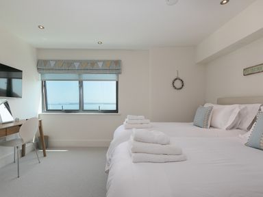 A bedroom with two beds with towels on them a desk with a chair and a window with a view at Crystal Bay in St Ives