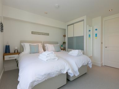 A bedroom with two single beds side by side with white bedding and folded towels on top at Crystal Bay in St Ives