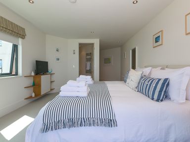 A bedroom with a bed with striped bedding and folded towels a wall-mounted shelf with a television and decorative items at Crystal Bay in St Ives